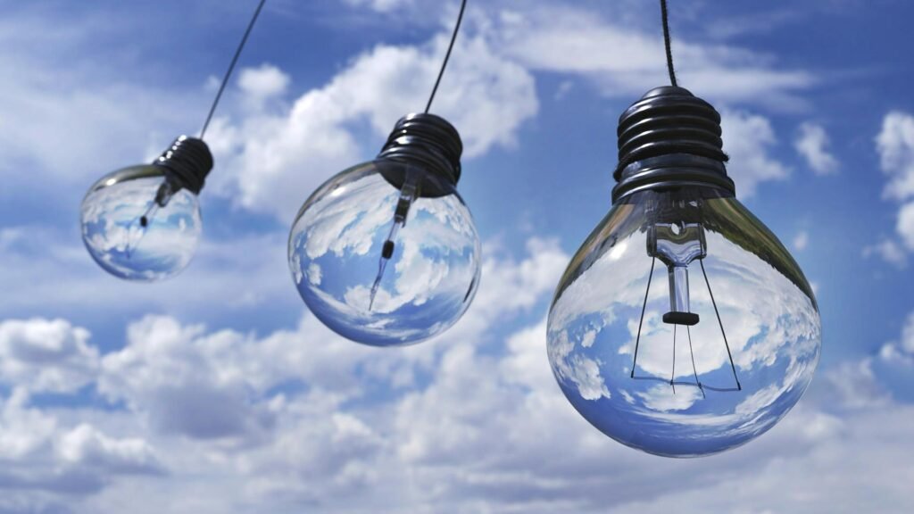 Surreal image of light bulbs reflecting blue sky and clouds, symbolizing creativity and energy.